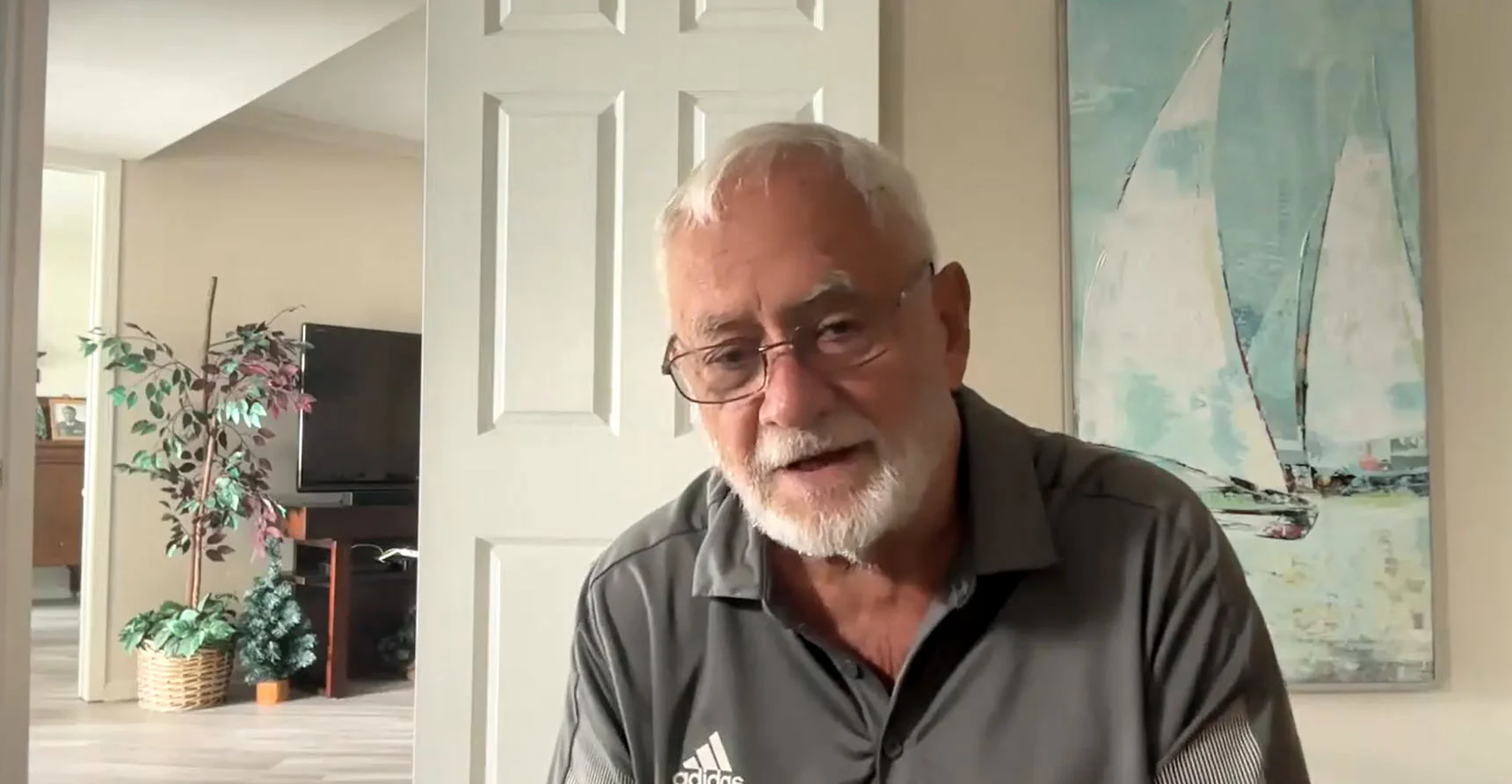 Jim Fisher in front of an open white door and a painting of 2 sailboats